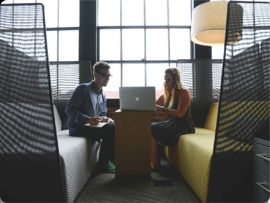 A consultant and a client reviewing notes over a laptop in an office booth during a diagnosis session.