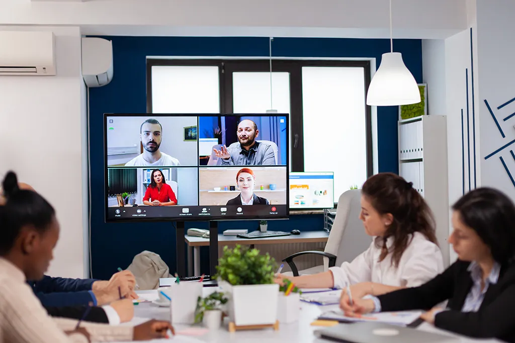 A meeting room team on a video call with four remote colleagues on the display.