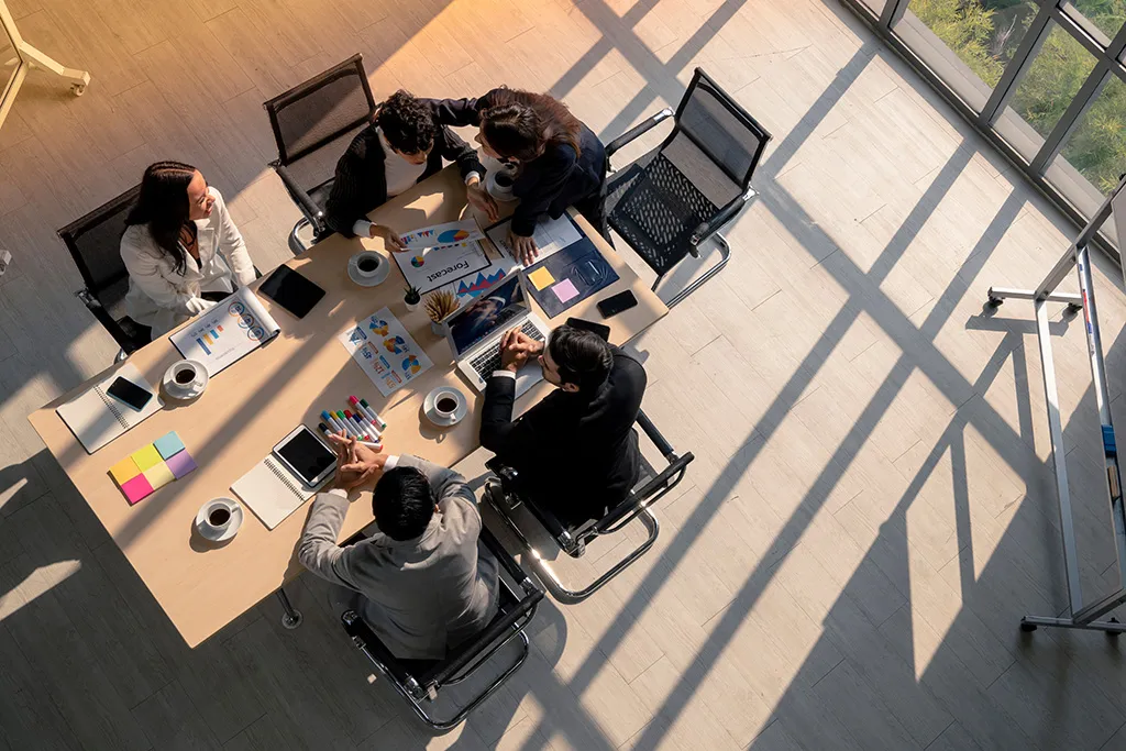 Overhead view of four colleagues reviewing forecast charts across a meeting table.